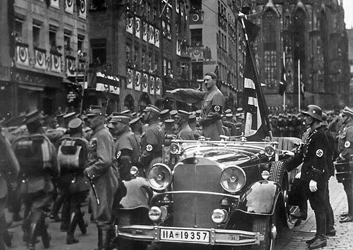 Parade of SA troops past Hitler. Nuremberg, in the car with Hitler: the en:Blutfahne, behind the car SS-man en:Jakob Grimminger the carrier of the Blutfahne flag.