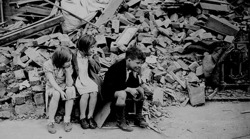 Children in the east end of London, made homeless by the random bombs of the Nazi night raiders, waiting outside the wreckage of what was their home. September 1940