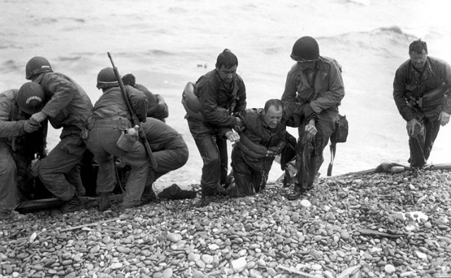Survivors of a sunken troop transport wade ashore on Omaha Beach.