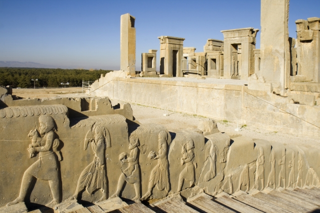 Bas-relief decoration along stairs from Darius palace to Palace of Xerxes, ruins of Daraius palace on the background.